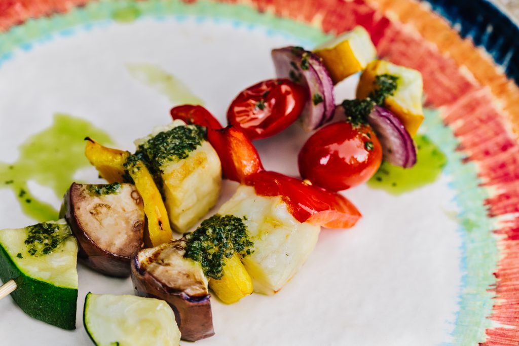 multi color vegetable BBQ skewers with green pesto on white plate