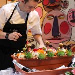 chef tom infront of a wall with faces painted on with colorful food and flowers